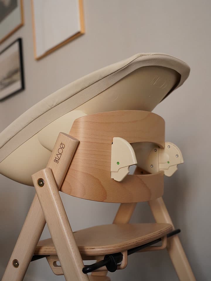 KLAPP Wooden high chair with a Newborn seat, set against a neutral wall with framed artwork.